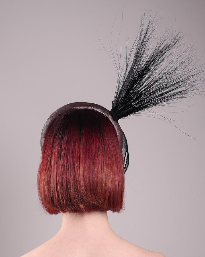 The model showcases the back of the Zephyr grey velvet headband with the hand-shaped wire black glove fitted with crinoline cascades dramatically across the face, balanced by a bursting spray of sleek horsehair. Designed by Merve Bayindir.