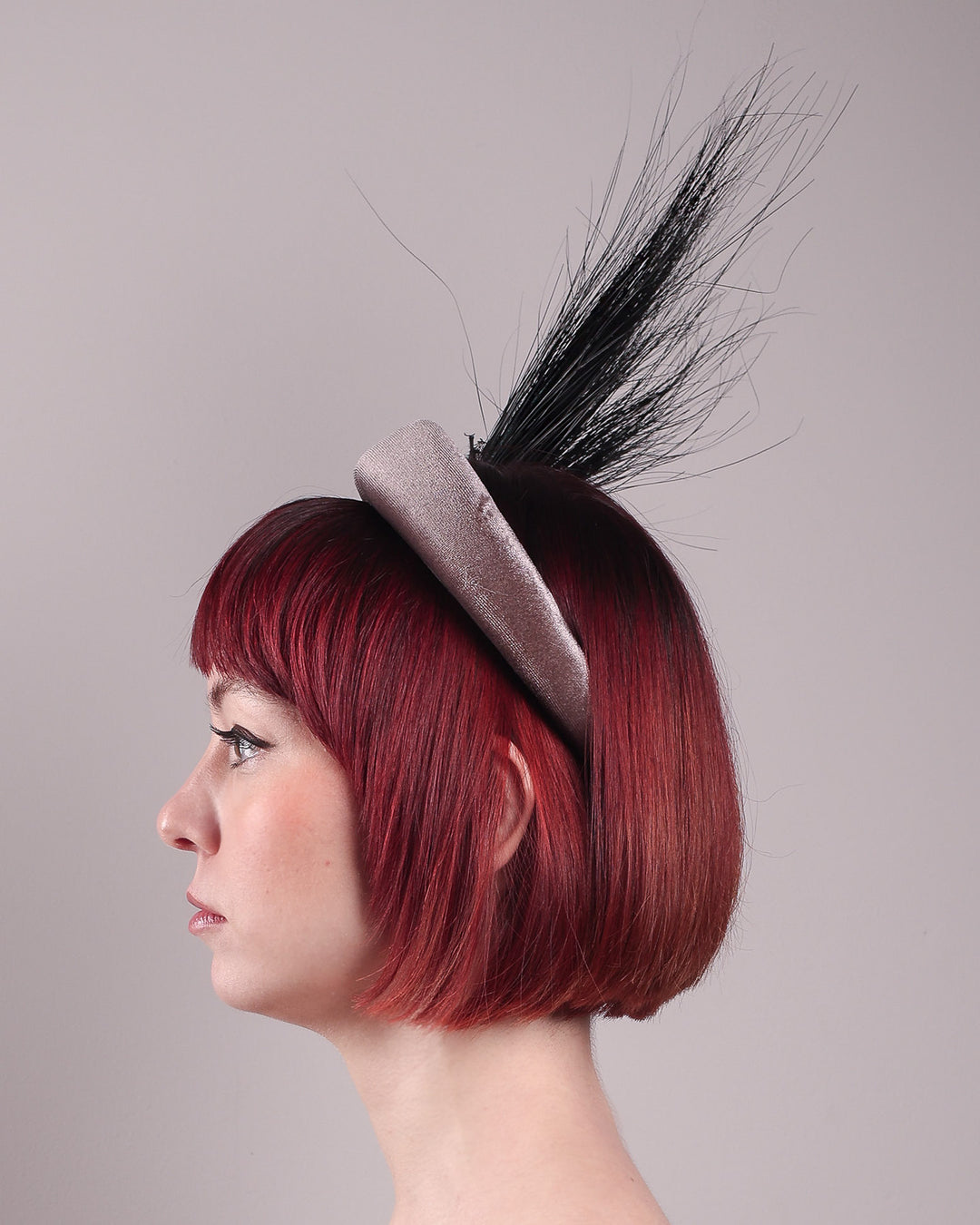 The model showcases the left side close up of the Zephyr grey velvet headband with the hand-shaped wire black glove fitted with crinoline cascades dramatically across the face, balanced by a bursting spray of sleek horsehair. Designed by Merve Bayindir.