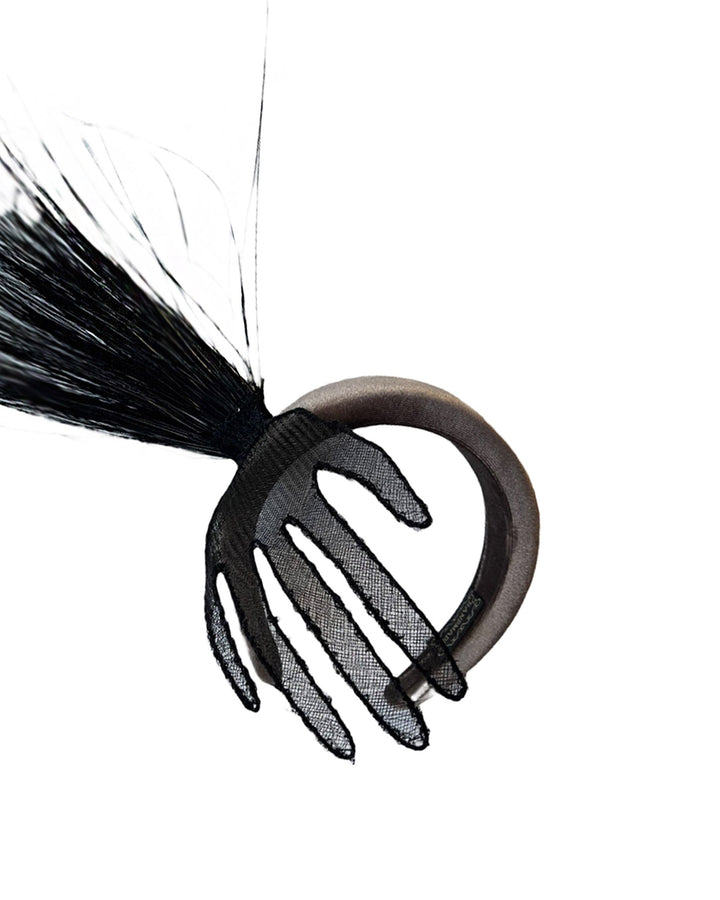 Still life picture of the Zephyr grey velvet headband with the hand-shaped wire black glove fitted with crinoline cascades dramatically across the face, balanced by a bursting spray of sleek horsehair. Designed by Merve Bayindir.