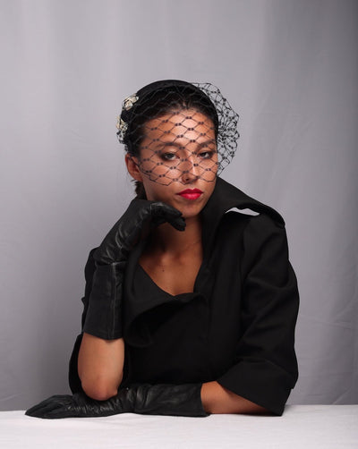 Model wearing a black sateen half hat with a black waffle style veil covering half of the face. 