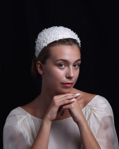 The model wears a custom-shaped bridal headpiece embellished with small organza flowers and pearl beads. From the front, the headpiece looks like a headband. From the back, it has three edges that hold the head. The vintage-style headpiece is perfect for classic brides.