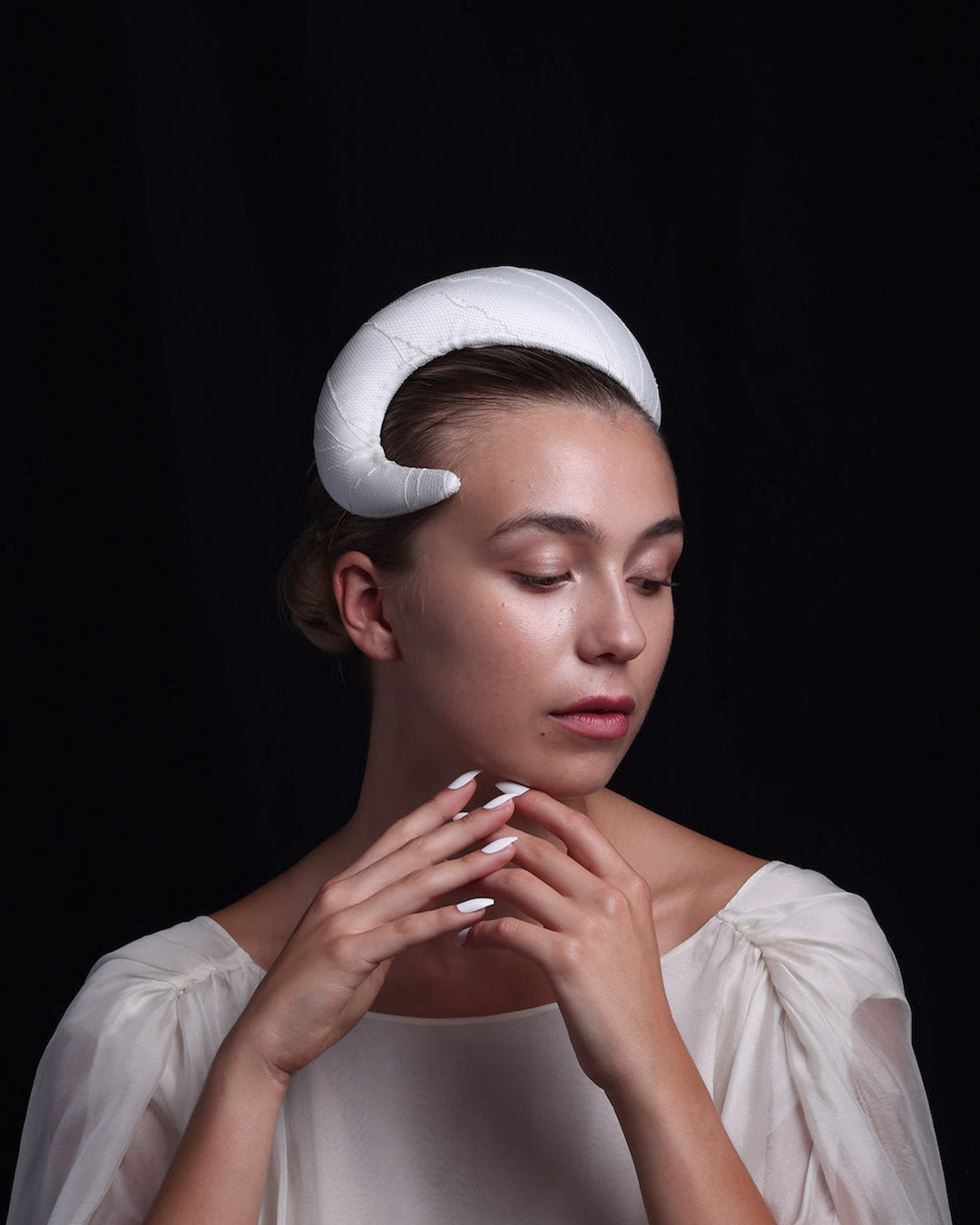 The model showcases an “S” shaped sateen bridal headband covered with a sheer tulle with glitter. The piece starts from the right side and curves upwards, head-hugging the head while getting thicker.  The artistic headband is perfect for modern brides.