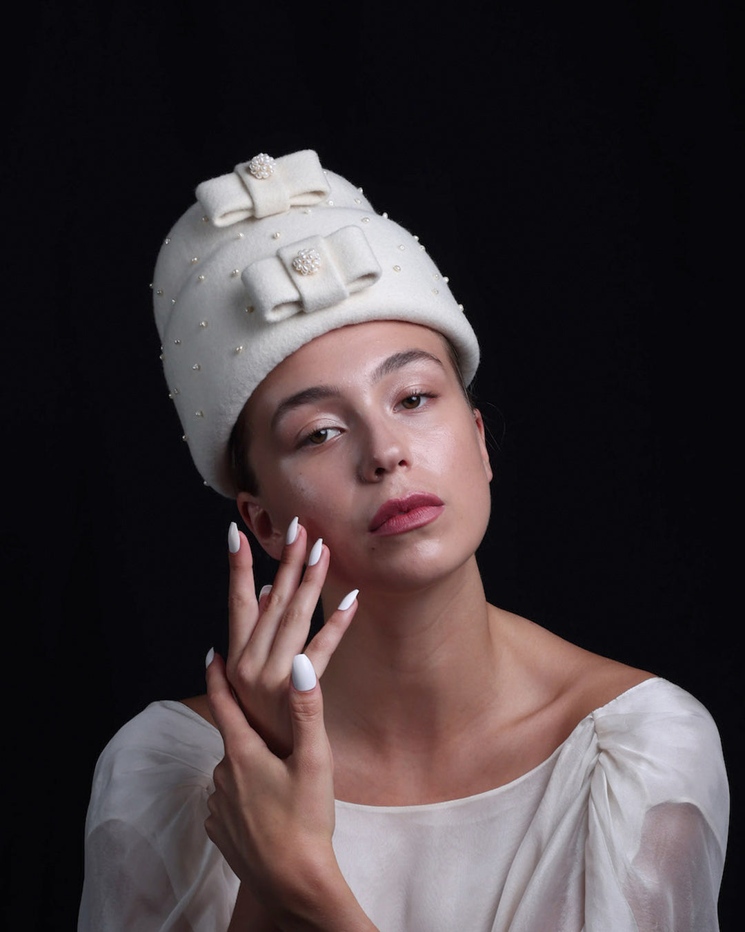 Model is wearing a double layer, tall ivory pillbox hat embellished with pearls.. The hat has ove ivory felt bow on each later, centres adorned with pearl balls. 