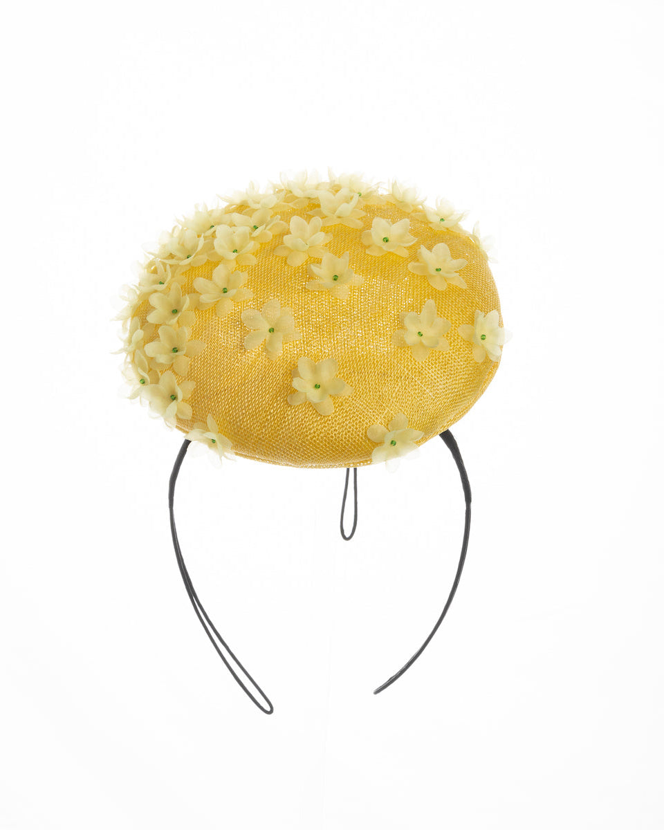 Yellow button shaped fascinator, decorated with yellow organza flowers and green beads. Designed and made by Merve Bayindir Millinery.
