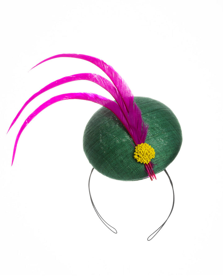 Emerald green button shaped fascinator decorated with with 3 hot pink trimmed feathers crossing the centre of the hat and yellow bead balls at the edge of the feathers. Designed and made by Merve Bayindir millinery.