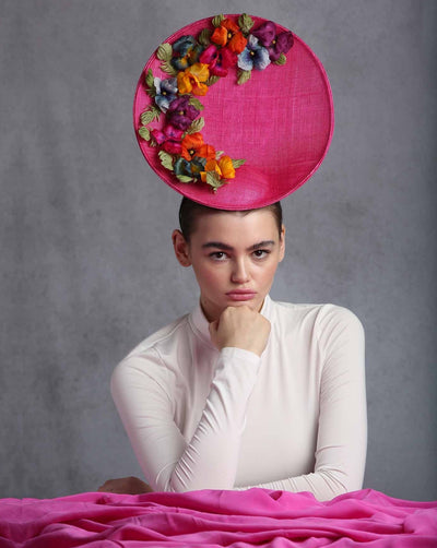 The model is wearing a large size oval shaped hot pink fascinator decorated with custom made silk organza multi-coloured violets