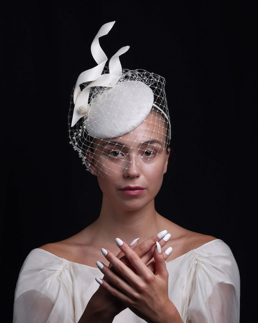 Model is showcasing a white button shaped bridal fascinator decorated with two buntal swirls and rounded with mother of pearl embroidered veil.