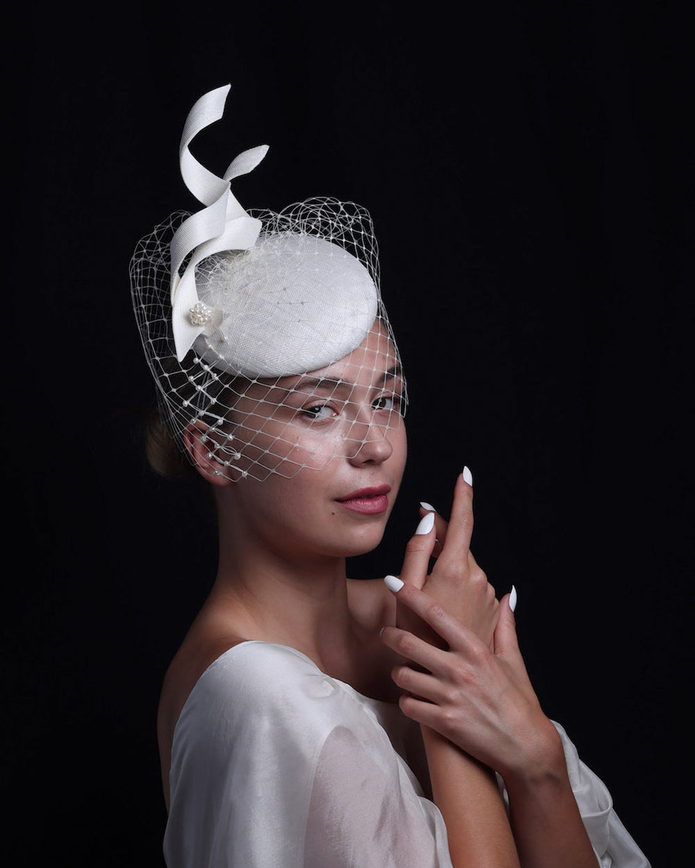 Model is wearing a white button shaped bridal fascinator decorated with two buntal swirls and rounded with mother of pearl embroidered veil.