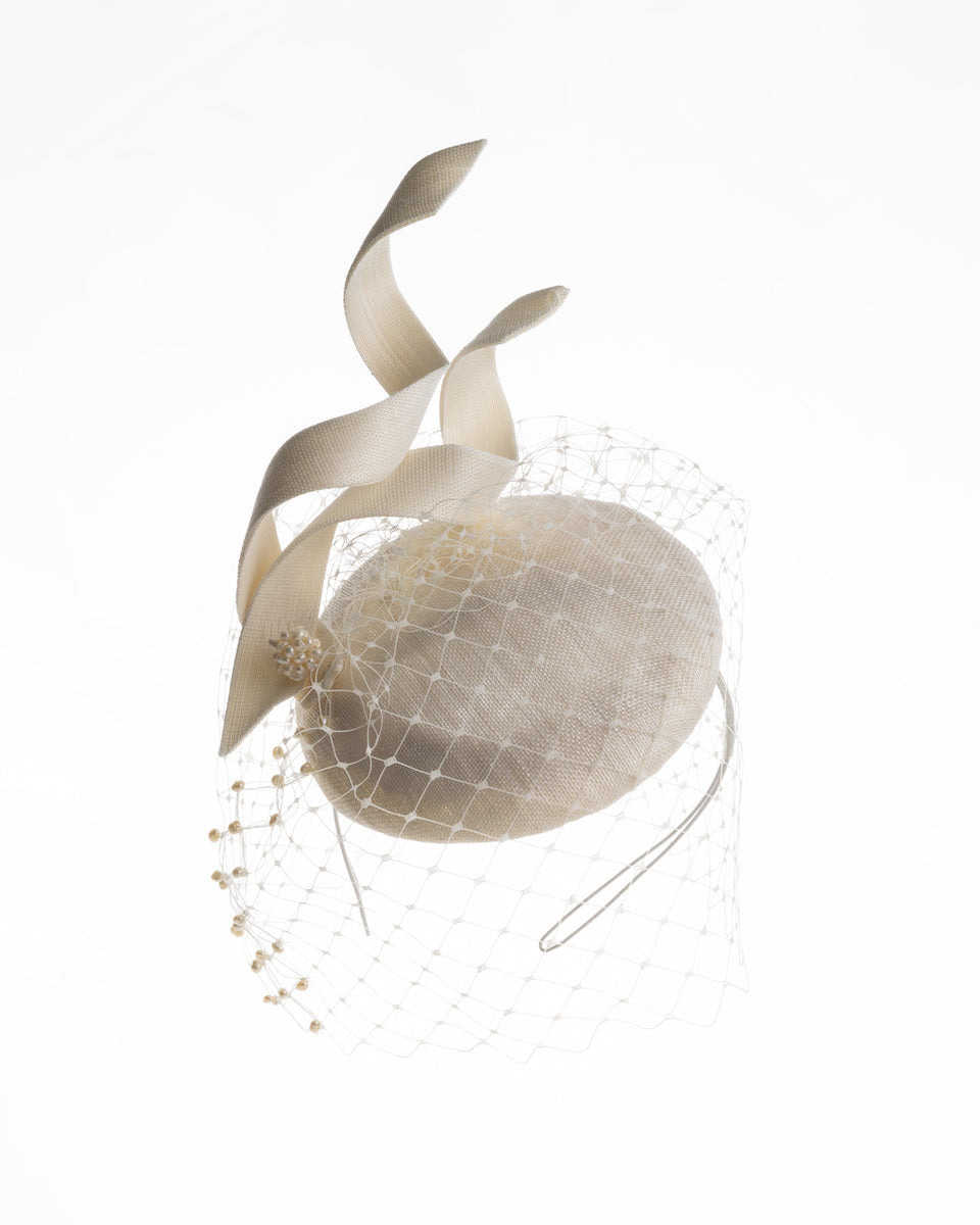 A white button shaped bridal fascinator decorated with two buntal swirls and rounded with mother of pearl embroidered veil.