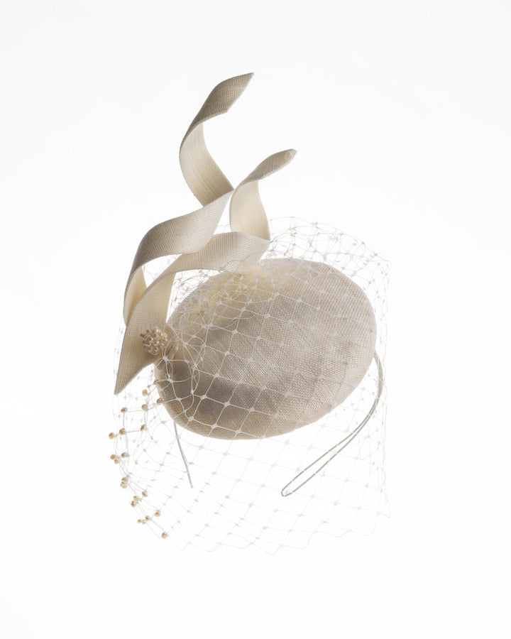 A white button shaped bridal fascinator decorated with two buntal swirls and rounded with mother of pearl embroidered veil.