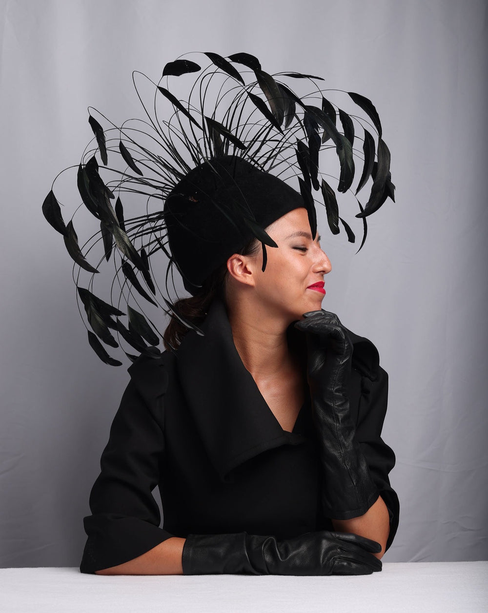 Model is showcasing Tall double pillbox felt base decorated with long Chanel style feathers surrounding the hat