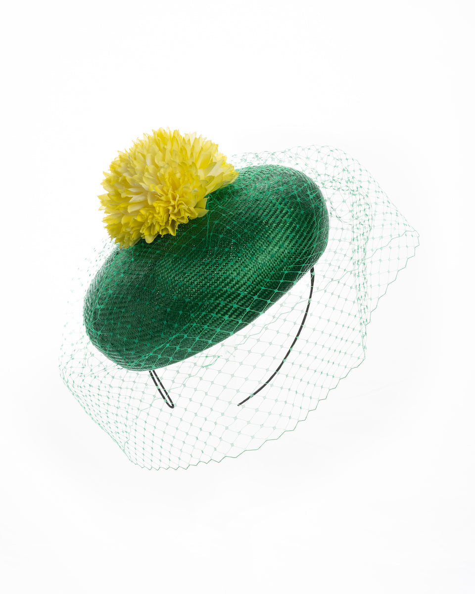 Emerald green summer beret tilted to the right side of the head, the vibrant headpiece is rounded with a delicate emerald green veil and completed with a bright yellow pompom flower on top. Designed and made by Merve Bayindir millinery.