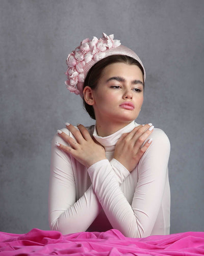 Model is showcasing the rich side of a pink parasisal pillbox hat with pink flowers