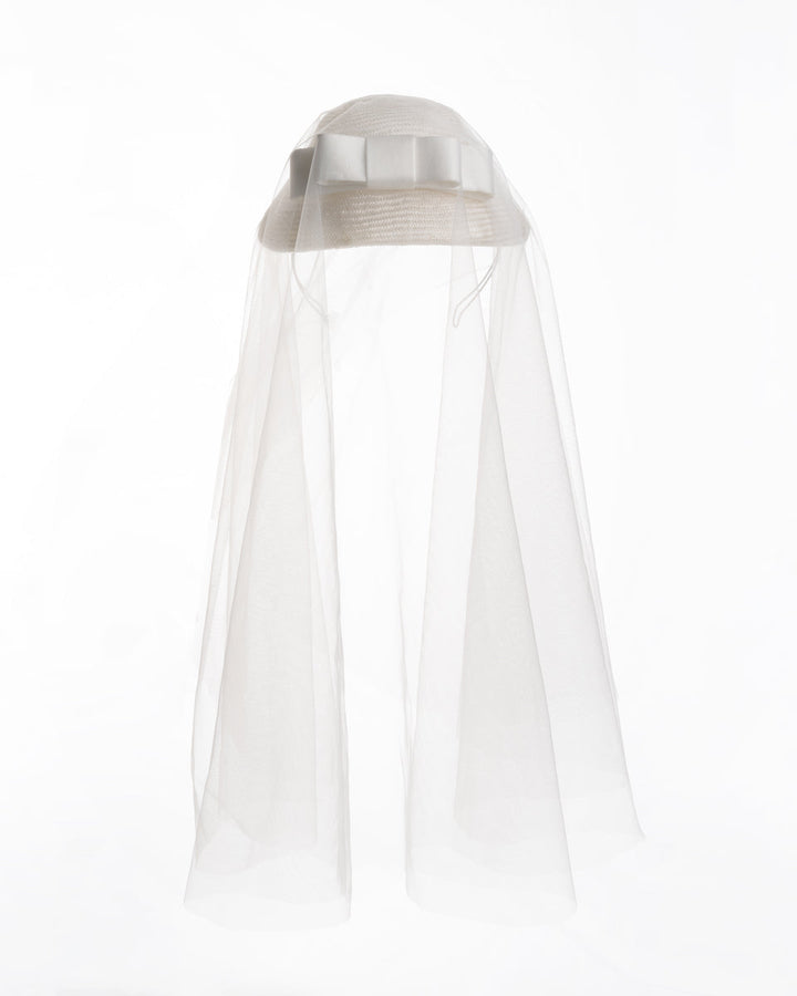 White curved, parasisal, pillbox style bridal headpiece decorated with a double layered sateen bow and completed with a shoulder length, circle ghost tulle veil.