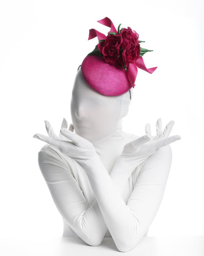 Model is showcasing the top of a button shaped hot pink button fascinator worn to the left front side of the head, this vibrant fascinator is decorated with two hot pink buntal swirls and three large hot pink roses with green leaves.