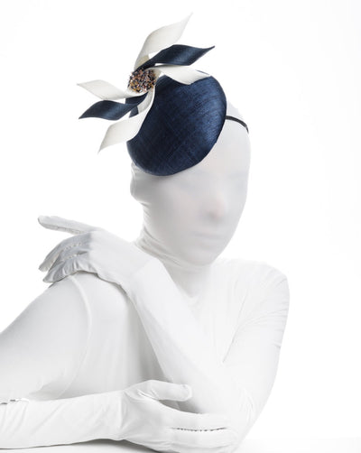 Model is wearing a navy, button shaped fascinator worn to the right side of the head. This chic headpiece is decorated with navy and white buntal swirls joined by multi coloured crystal beads, creating a flower-like silhouette.