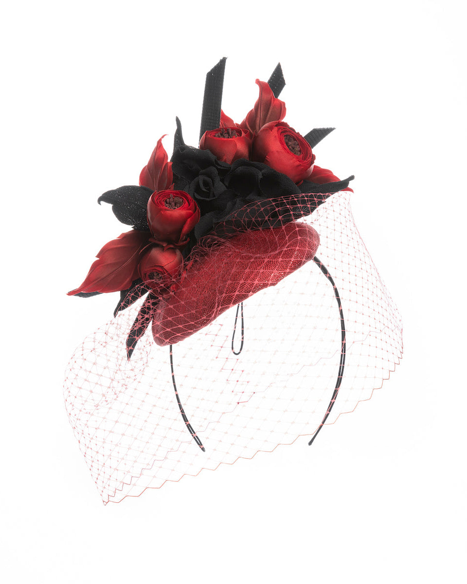A red button shaped fascinator worn to the centre to the right side of the head. This fascinator hat is decorated with a bouquet of black crepe roses, black shaded red peonies and black buntal swirls, and, rounded with a delicate red veil that covers the face. Designed and made by Merve Bayindir millinery.