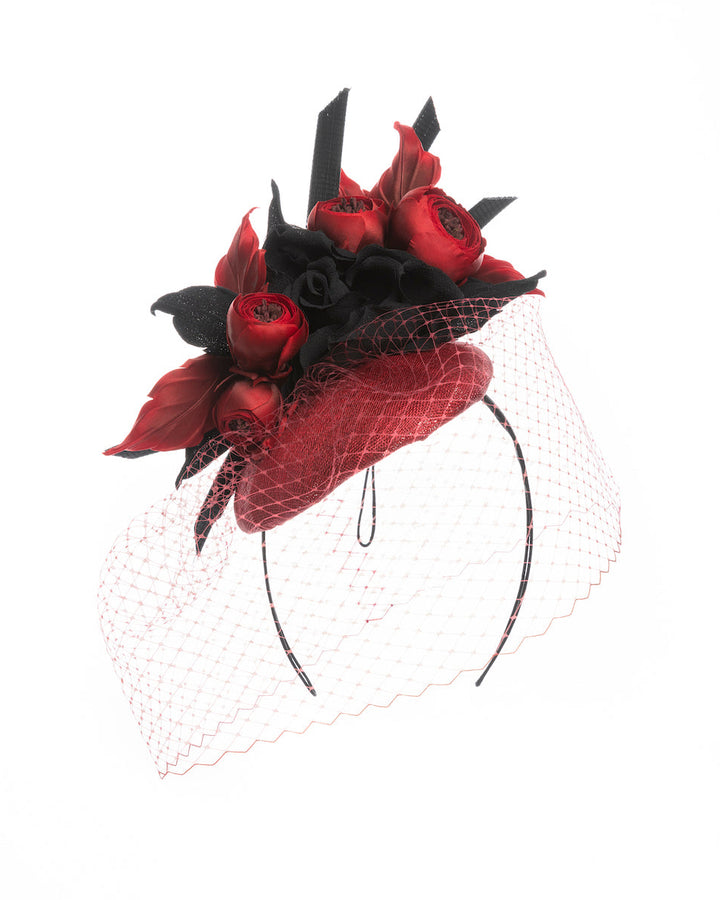 A red button shaped fascinator worn to the centre to the right side of the head. This fascinator hat is decorated with a bouquet of black crepe roses, black shaded red peonies and black buntal swirls, and, rounded with a delicate red veil that covers the face. Designed and made by Merve Bayindir millinery.