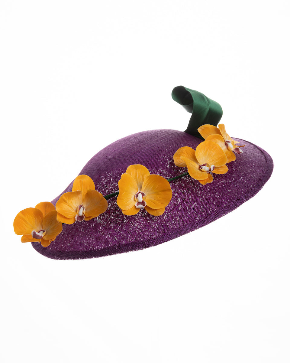  A deep purple, round sinamay saucer hat decorated with orange orchids and a green swirl leaf. Designed and made by Merve Bayindir Millinery.
