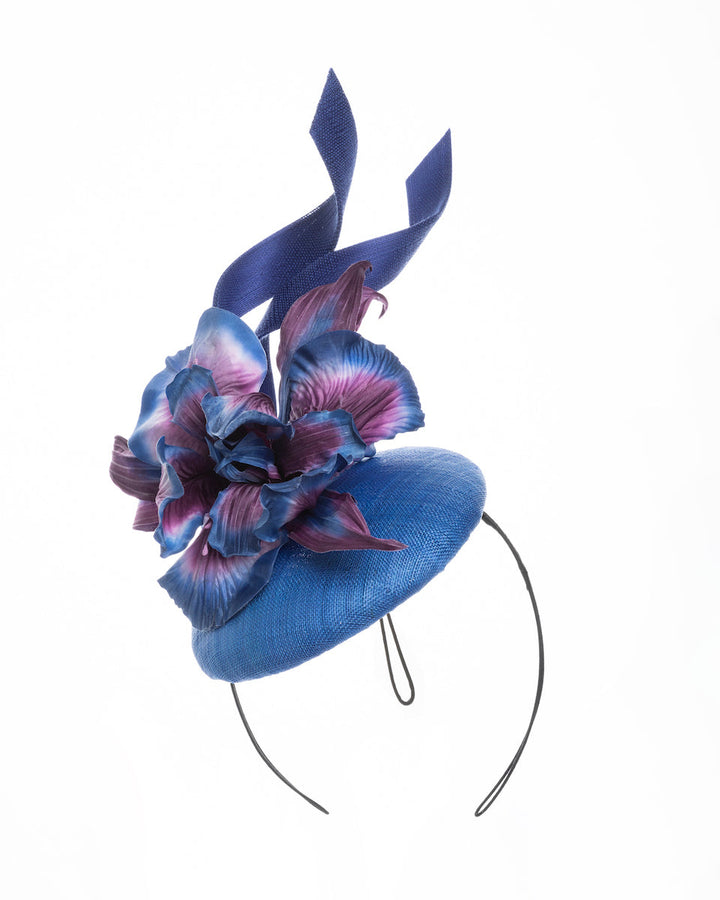 Deep blue button shaped fascinator decorated with colourful irises and two high buntal swirls. The flower is detailed in transitioning colour from deep blue to purple on iris petals. Designed and made by Merve Bayindir Millinery.
