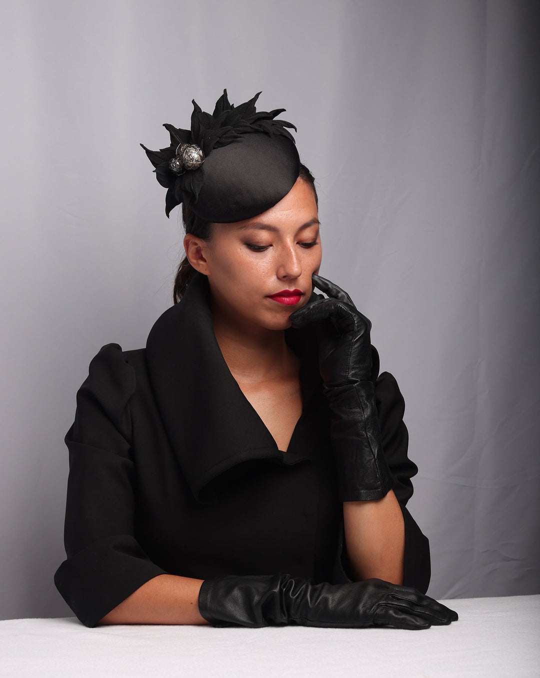 Model is showcasing The button style sateen based fascinator decorated with crepe leafs and centred with wire embellished plastic large pearls. The fascinator sits on the right front side of the head.
