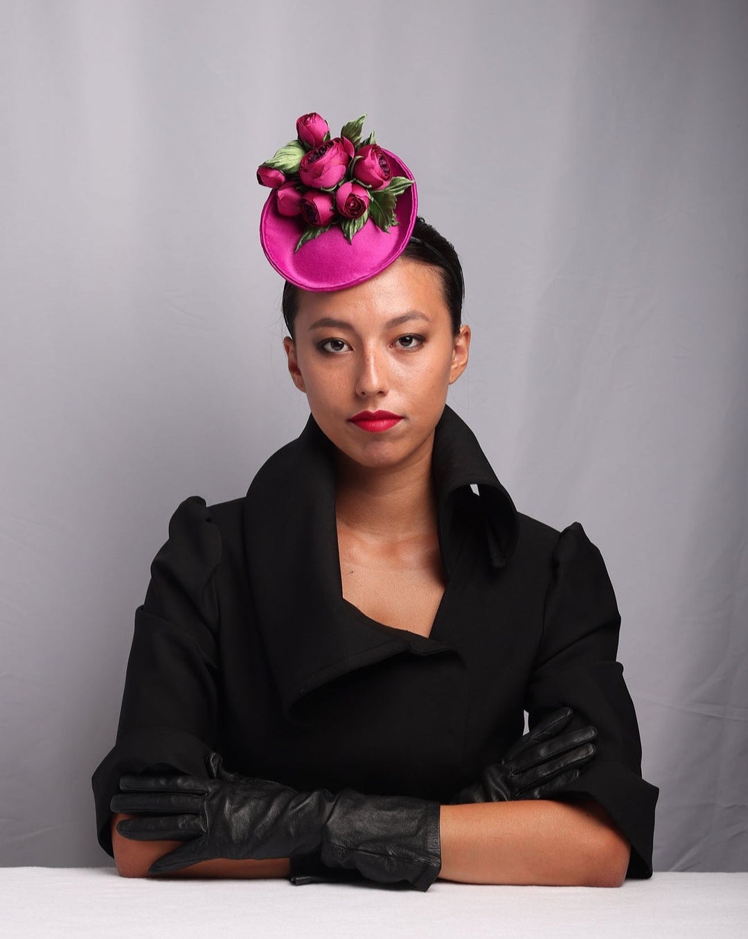 The model is showcasing the front look of a small fascinator sitting on the front right side of her head. Small saucer style pink sateen fascinator, embellished sateen wild rose bouquet.