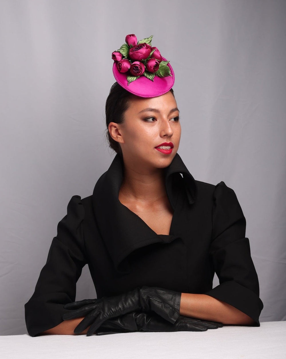 The model is showcasing the side of a Small saucer style pink sateen fascinator, embellished sateen wild rose bouquet.