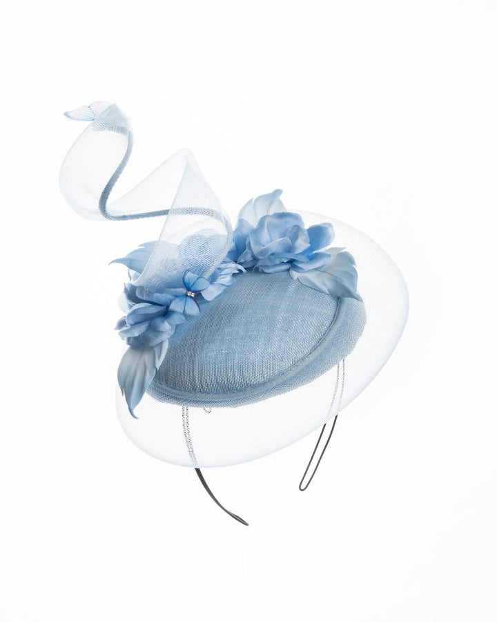 Light blue button shaped fascinator. This unique fascinator is circled with light blue crinoline and is decorated with blue roses, shaded blue leaves and blue organza butterflies. Designed and made by Merve Bayindir Millinery.
