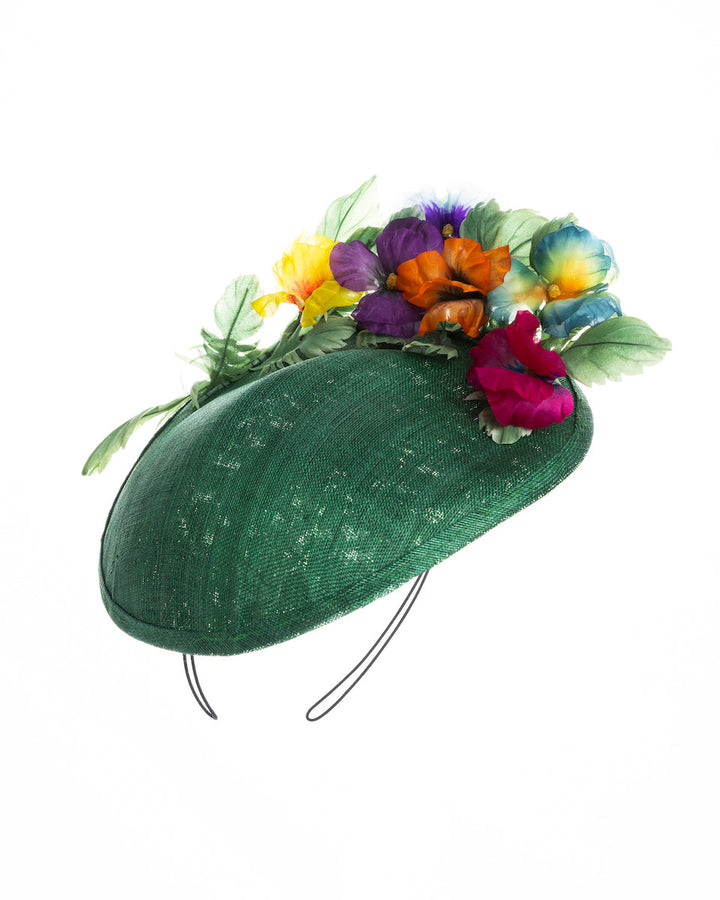 Still life picture of small, asymmetric emerald green saucer hat decorated with multi coloured violets on the left. Created and designed by Merve bayindir millinery.