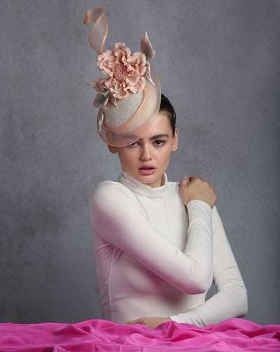 The model is showcasing Button shape sinamay fascinator, the base rounded with crinoline that swirls upwards at the back, decorated with custom made peach colour crepe wild rose. The fascinator sits on the right front side of the head.