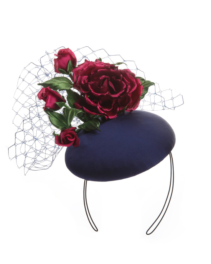 Sateen button shaped fascinator, decorated with dark pink sateen roses embellished with green leaves and navy veil.