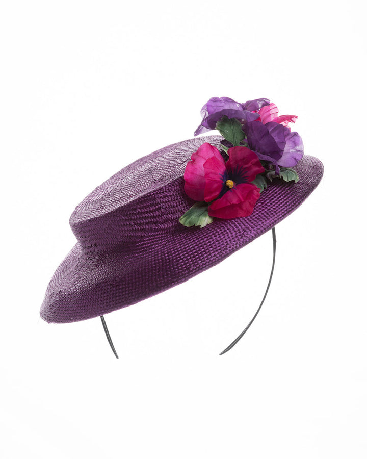 Purple parasisal mini boater hat decorated with purple and hot pink violets on the left side. Worn to the right side of the head. Designed and made by Merve Bayindir Millinery.
