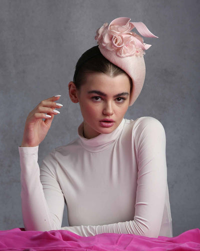 The model is showcasing the left view of a Pink Sinamay teardrop shape side fascinator.Decorated with custom made silk sateen flowers and jinsin swirls on the top.