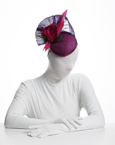 Model is showcasing the right top view of a a purple sinamay button shaped fascinator decorated with curved silk abaca fabric curving like a sea shell, two buntal swirls and a large pink silk rose, exemplifying the harmony of different shades of color.