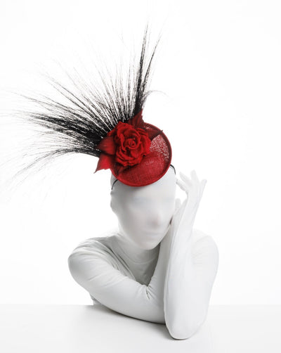 Model is showcasing Mini red saucer fascinator, adorned with a red rose embellished with high rising black burnt peacock feathers.