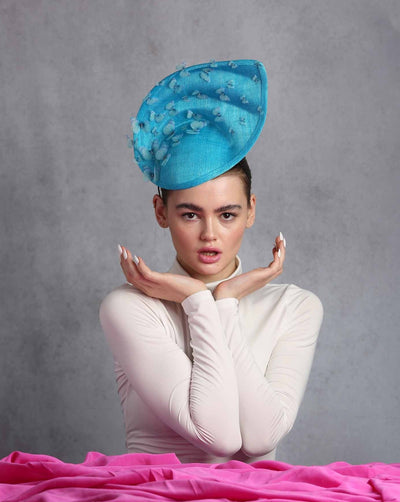 Model is showcasing the top view of a High top asymmetric shell looking teal colour sinamay fascinator decorated with silk organza butterflies